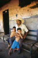 Acompanied by two little ones, a Balsamo campesino rests on the porch of his ranch.